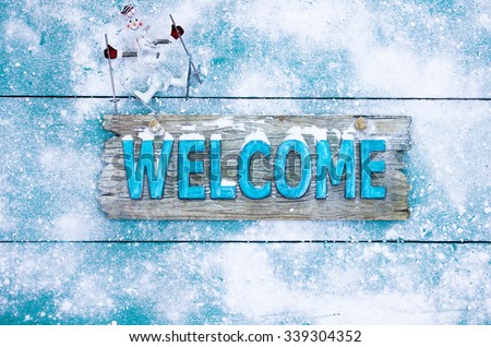 Winter welcome sign with snowman skier on teal blue snowy wooden background