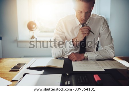 Serious business man working on documents looking concentrated with briefcase and phone on the table Royalty-Free Stock Photo #339364181