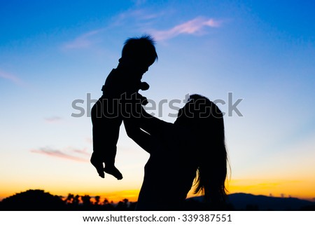 a silhouette picture of mother holding her baby while the sunset and twilight sky.