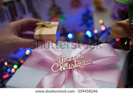 Image gift that says "Merry Christmas" in the rays blurred festive lights. The picture is a Christmas present in hand on a background of colored lights garlands.
