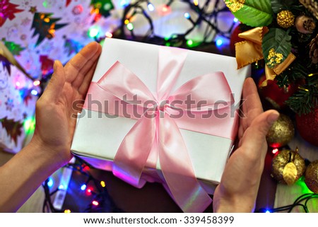 Image gift "Merry Christmas" in the rays blurred festive lights and Christmas tree decorations. The picture is a Christmas present in hand on a background of colored lights and Christmas decorations.