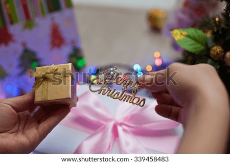 Image of the gift and the inscription "Merry Christmas" in the rays blurred festive lights. The picture is a Christmas present in hand on a background of colored lights garlands.