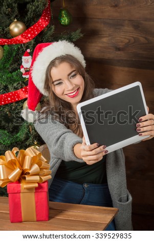 New Year and Christmas concepts. Beautiful girl making selfies on her tablet PC near New Year tree at home atmosphere.