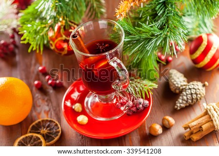 Glass of traditional hot drink on table by Christmas tree with decorations. Mulled wine.
