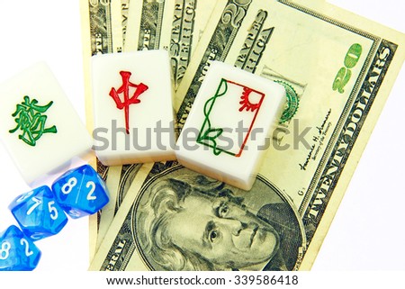 Mahjong gaming tiles with Chinese characters and symbols of green luck, red dragon and paper window on a stack of US currency for the concept of China betting in USA.