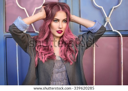 Beautiful hipster fashion model with curly pink hair posing in front of the colorful wall Royalty-Free Stock Photo #339620285
