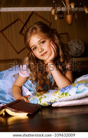 Little girl in a blue dress lies on the floor in room, beside her is a book