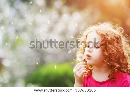 Little curly girl blowing dandelion. Royalty-Free Stock Photo #339633185