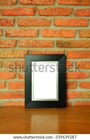 Black picture frame on the old brick wall and the wooden floor background