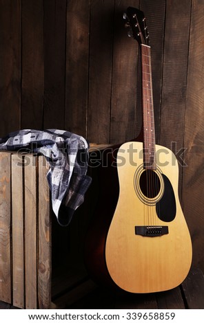 Guitar and shirt left on crate on wooden wall background