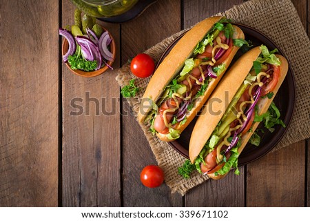 Hot dog with  pickles, tomato and lettuce on wooden background. Top view Royalty-Free Stock Photo #339671102
