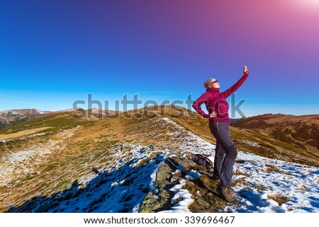 Cute Woman in sporty Clothing making self portrait on mobile Phone Mountains View and Sun Shining