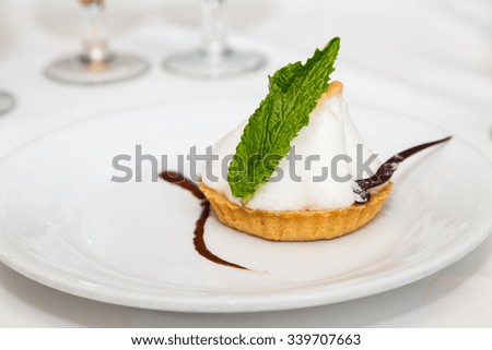 A tart topped with meringue and garnished with chocolate and a mint leaf