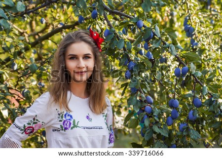 Portrait of beautiful young female posing in traditional Serbian clothing near a plum tree