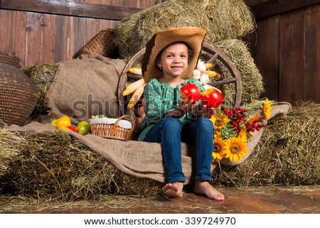 Smiling little african girl in cowboy hat sitting in the hay with apples