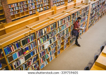 Student reading a book from shelf in library at the university