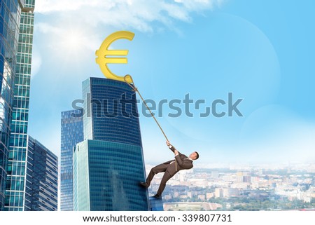 Businessman climbing skyscraper holding golden euro sign