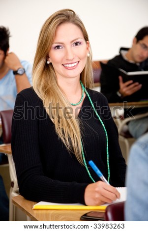 Beautiful girl studying in the classroom - smiling and writting on her notebook