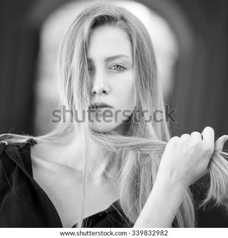Closeup portrait of one beautiful serious cool blonde young woman with long hair outdoor looking forward on blurred background black and white, square picture