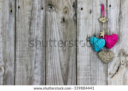 Brass skeleton key with Love and teal blue and pink rope hearts hanging on antique rustic wood background