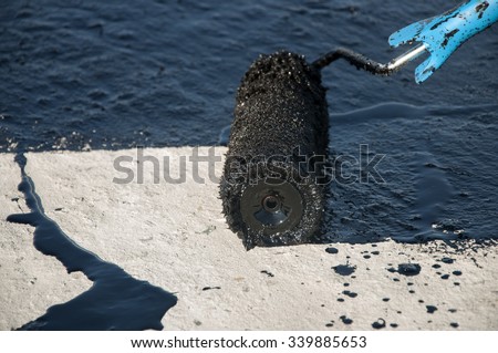 Roofer worker painting black coal tar or bitumen at concrete surface by the roller brush,   waterproofing Royalty-Free Stock Photo #339885653