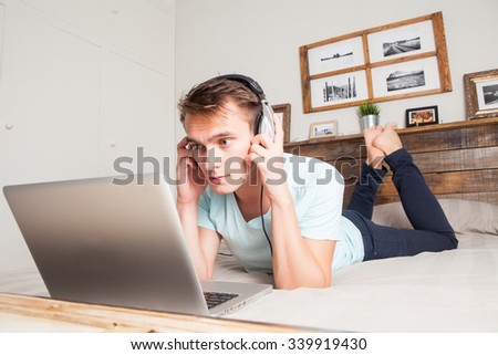 White man listening music from a computer with headphones at home lying down on the bed