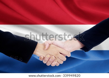 Image of two people in business suit, shaking hands in front of Netherlands national flag