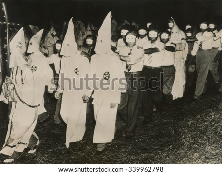 Ku Klux Klan initiation at Stone Mountain near Atlanta, Georgia. June 1949. KKK men in full white masks and gowns lead new members wearing small face masks Royalty-Free Stock Photo #339962798