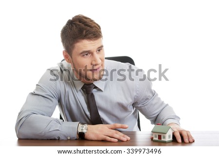 Happy businessman with house model by a desk.