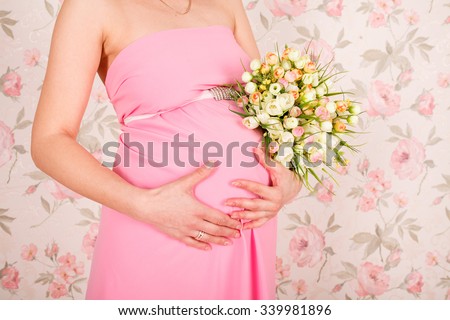 Pregnant woman holding her belly and flower, pink studio background.