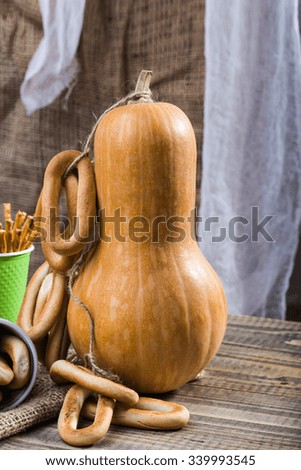 Still life closeup one big gourd with bunches of hard oval cracknels bind with string partial disposable green cup with straws standing on wooden table on blurred rustic background, vertical picture 