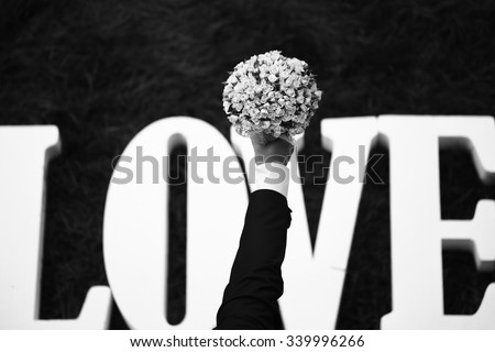Closeup view of one beautiful fresh bright white yellow big wedding bouquet of rose flowers in human hand of bride and love text of letters lying on green grass, horizontal picture