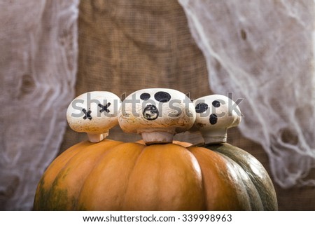 Photo closeup autumn still life part of one big whole fresh orange pumpkin with three Halloween champignons with ghost faces drawn in black on top on blurred rustic background, horizontal picture