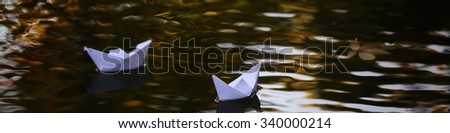 Closeup view of beautiful colorful autumn tree leaves red yellow orange green colors floating on wavy water with reflection of nature with white paper ship on outdoor background, horizontal picture