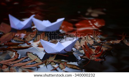 Closeup view of beautiful colorful autumn tree leaves red yellow orange green colors floating on wavy water with reflection of nature with white paper ship on outdoor background, horizontal picture