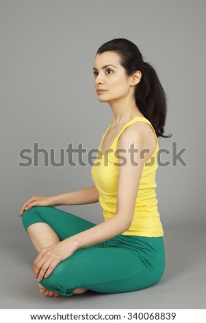 A young woman in exercise clothing sitting cross-legged looking away.
