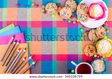 Fresh homemade muffins and cookies with color chocolate coated candies, colorful wooden pencils and notebooks, exercise books, cup of tea on a checkered kitchen towel. Free space for your text