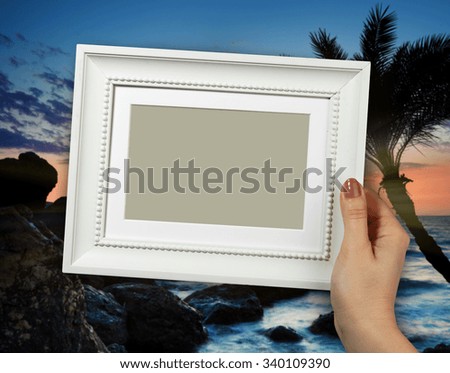 Wooden frame in beautiful woman hands on the background sunset at tropical beach
