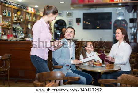 Attractive smiling waitress serving family of three at cafe table. Selective focus on girl