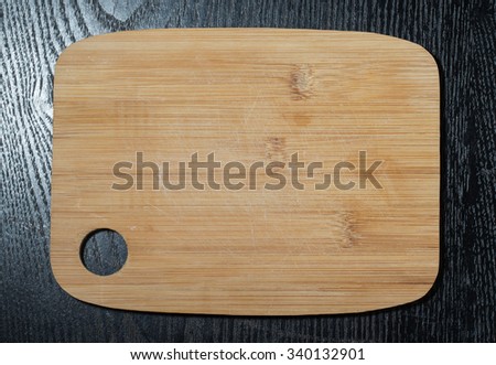 Modern light wooden cutting board with ring hole on a black table like background. Space for text.