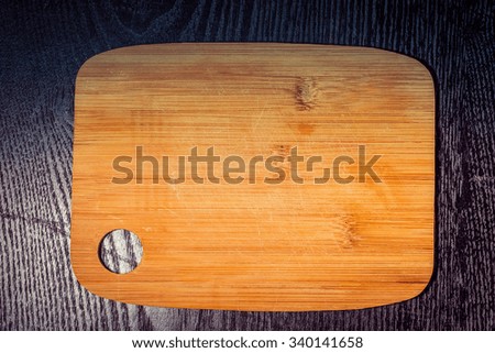Modern light wooden cutting board with ring hole on a black table like background. Space for text. Toned.