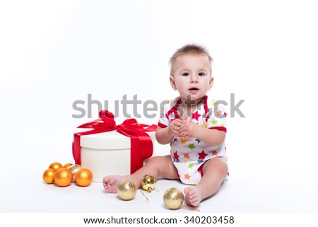 smiling baby sitting on the priest on a white background in white-red striped suit, surrounded by red and blue New Year's gifts and Christmas decorations.