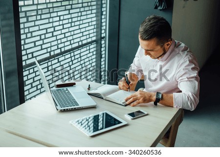 Young man sitting in cafe and adding new meeting in his calendar. Indoor photo