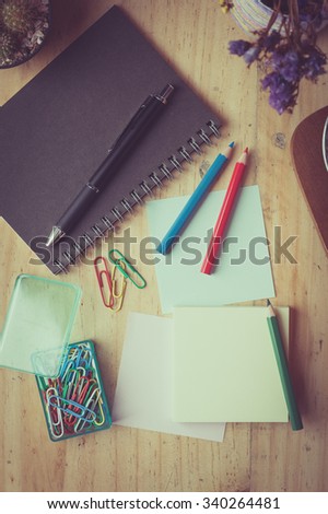 Sticky paper with blank space for text or message, notebook, paper clip, color pencil, and pen on wood table in cafe with vintage filter effect