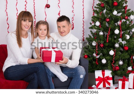 parents giving present to happy daughter in front of Christmas tree