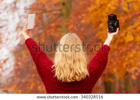 Pretty woman in fall forest park taking selfie self photo with old vintage camera and smartphone. Gorgeous young girl photographer. Autumn winter photography. Back rear view.