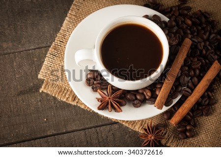 A white cup of coffee on wooden background with cinnamon and coffee beans.