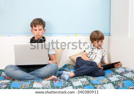 A two boys with a laptop and a tablet PC are sitting on the sofa