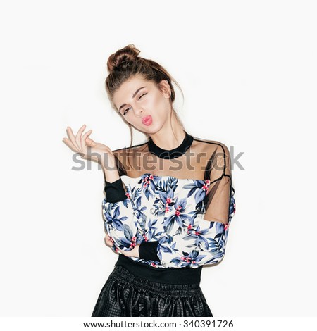 Portrait of young beautiful girl posing for camera. Bright makeup, top knot hairdo and casual style. White background, not isolated. Inside.