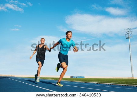 Shot of professional male athletes passing over the baton while running on the track. Athletes practicing relay race on racetrack. Royalty-Free Stock Photo #340410530